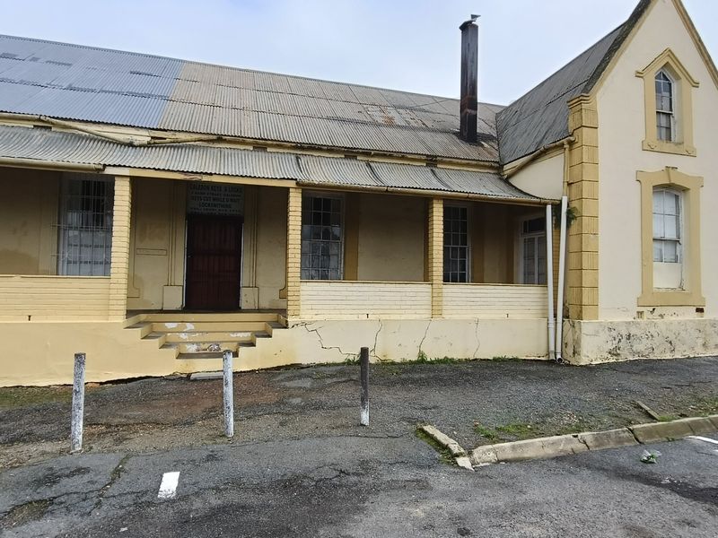 Front elevation of a historic-style building featuring a covered veranda, corrugated iron roof, and masonry walls showing signs of significant wear and structural cracking.