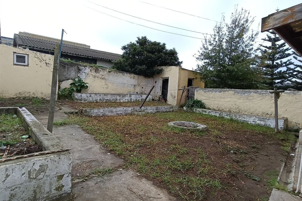 A rear garden area featuring concrete planter boxes, a paved path, and boundary walls requiring maintenance and landscaping to improve the outdoor space.