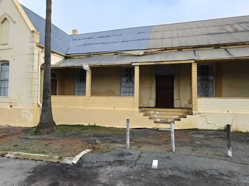 Front elevation of a historic-style building featuring a corrugated iron roof, covered veranda, and brick facade with visible signs of wear and structural weathering.