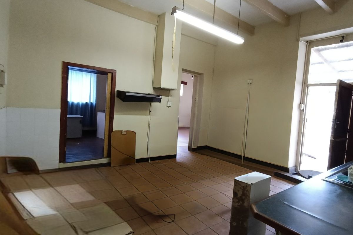 An empty, dated kitchen space featuring tiled flooring, exposed ceiling beams, and basic fixed infrastructure, offering significant potential for a modern renovation.