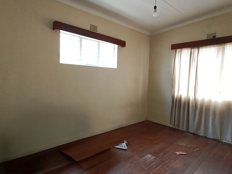 An empty bedroom featuring original timber flooring, timber curtain pelmets, and ventilation bricks, offering a blank canvas for renovation.