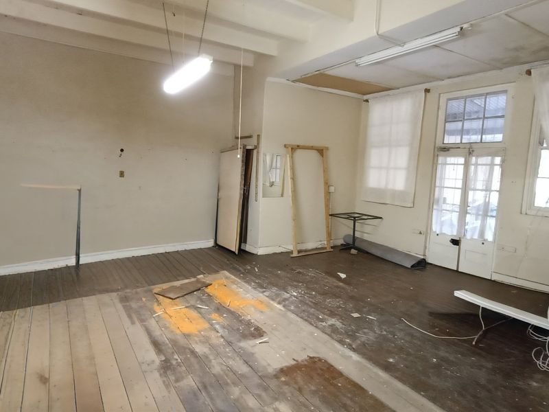 An empty, dated living room featuring exposed timber floorboards, ceiling beams, and french doors, requiring significant renovation and cosmetic updates.