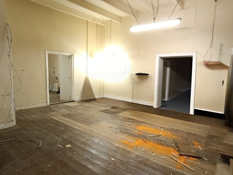 An empty living area featuring original timber flooring, exposed ceiling beams, and built-in cabinetry, currently requiring significant renovation and cosmetic updates.