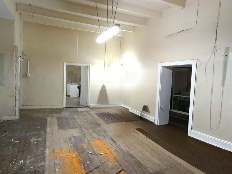 An empty, unfinished living area featuring exposed timber flooring, high ceilings with exposed beams, and multiple internal doorways requiring renovation.