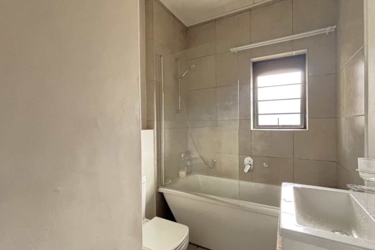 A functional bathroom featuring a bathtub with a glass shower screen, a wall-mounted toilet, and a modern vanity basin with tiled wall finishes.