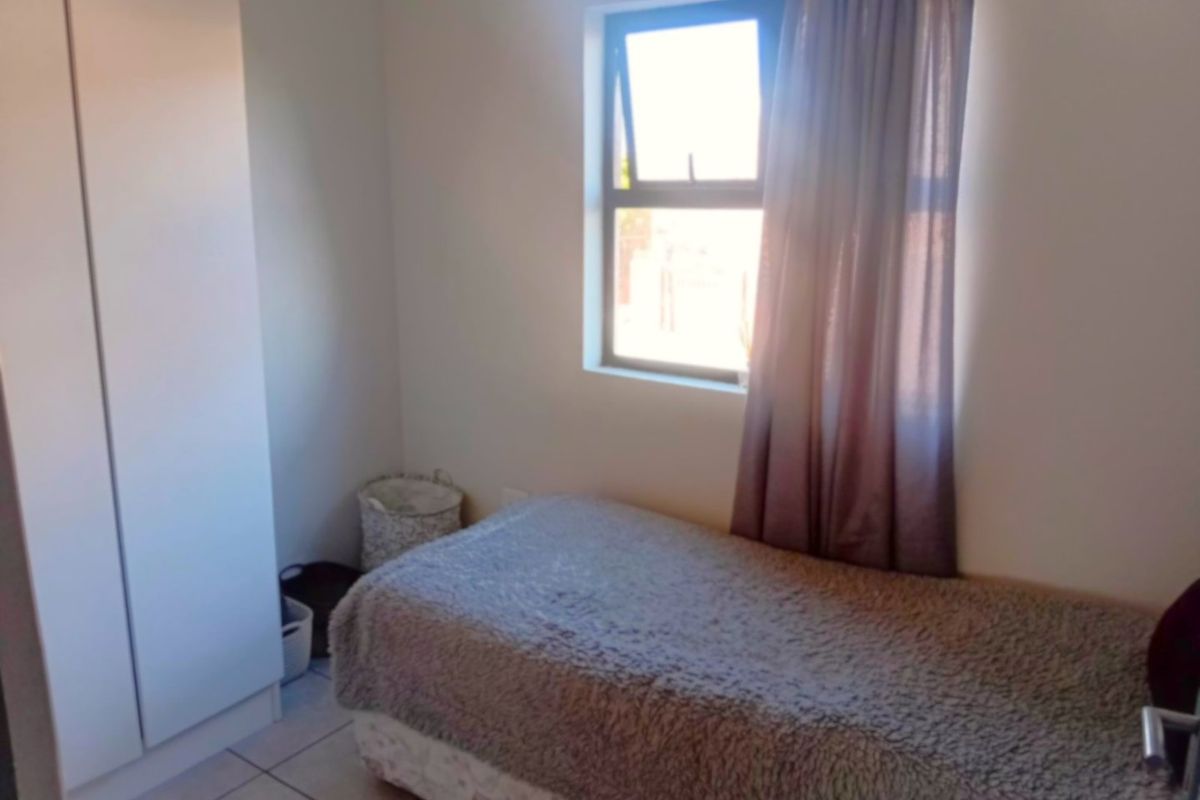 A functional bedroom featuring tiled flooring, a built-in wardrobe, and a window providing natural light.