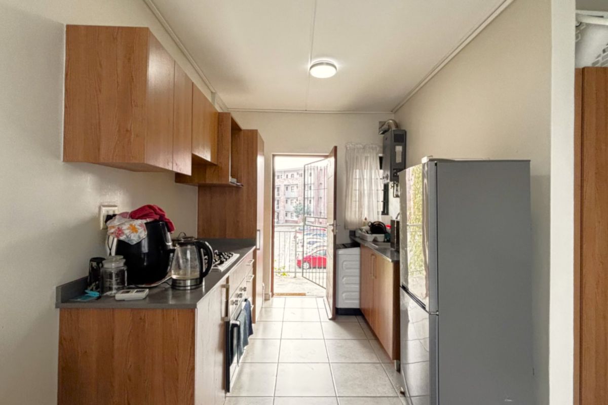 A functional galley-style kitchen featuring laminate cabinetry, stone-look countertops, built-in oven and hob, and direct access to an exterior balcony.
