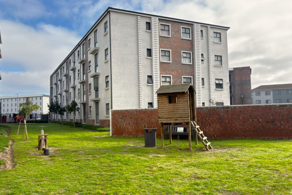 A view of the rear exterior of a multi-story apartment complex featuring a communal lawn area and brick boundary wall.