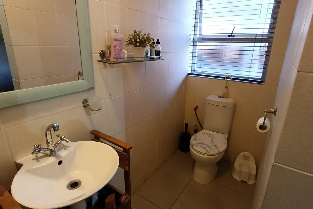 A functional bathroom featuring tiled walls, a pedestal basin with chrome fixtures, and a standard toilet with natural light from a window.