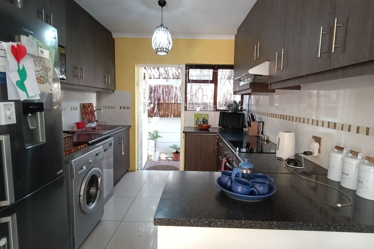 A functional kitchen featuring dark wood cabinetry, granite-look countertops, tiled flooring, and a tiled backsplash, with direct access to an outdoor area.