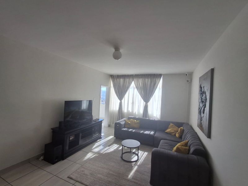 A functional living room featuring neutral tiled flooring and natural light through large window curtains, providing a comfortable and versatile living space.