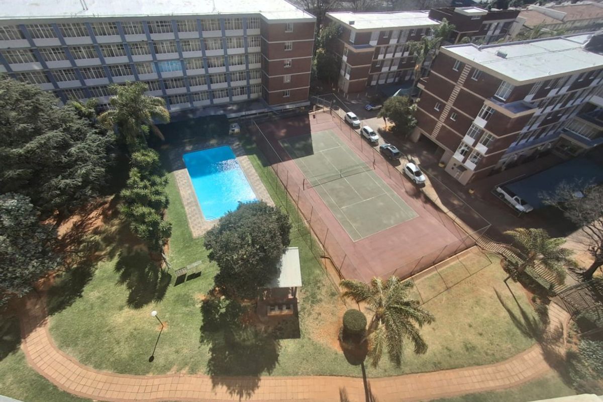 Aerial view of the apartment complex grounds featuring a swimming pool, tennis court, and landscaped garden areas.