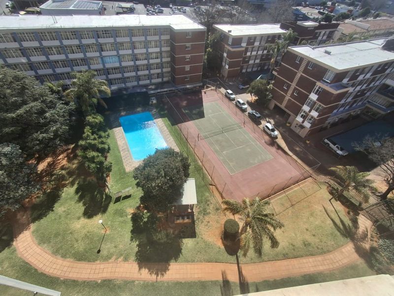Aerial view of the apartment complex grounds featuring a swimming pool, tennis court, and landscaped garden areas.