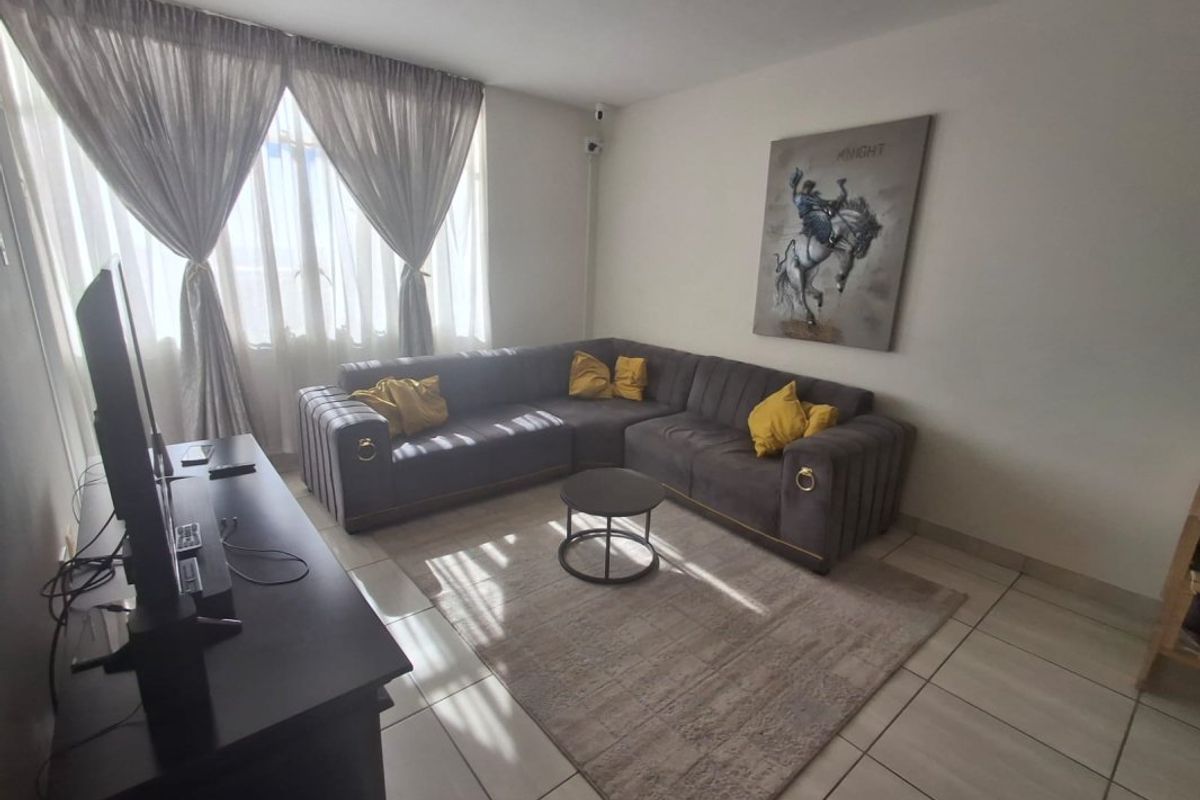 A living room featuring tiled flooring and large windows with curtain tracks, providing a functional space for relaxation.