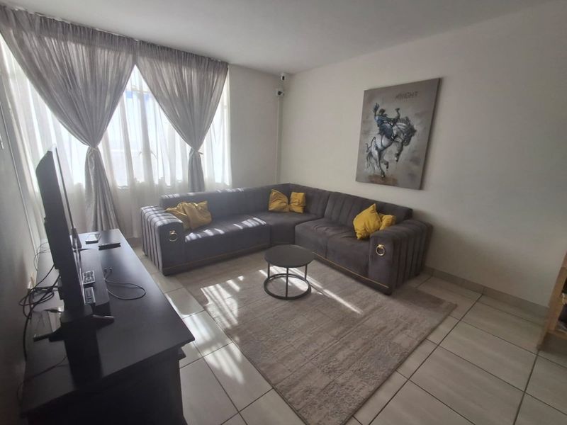 A living room featuring tiled flooring and large windows with curtain tracks, providing a functional space for relaxation.