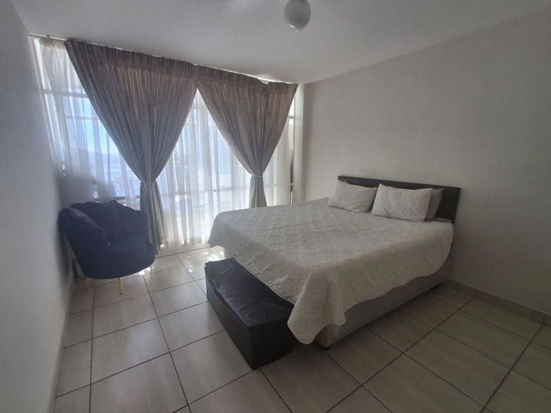 A spacious bedroom featuring large floor-to-ceiling windows that provide ample natural light and tiled flooring throughout.