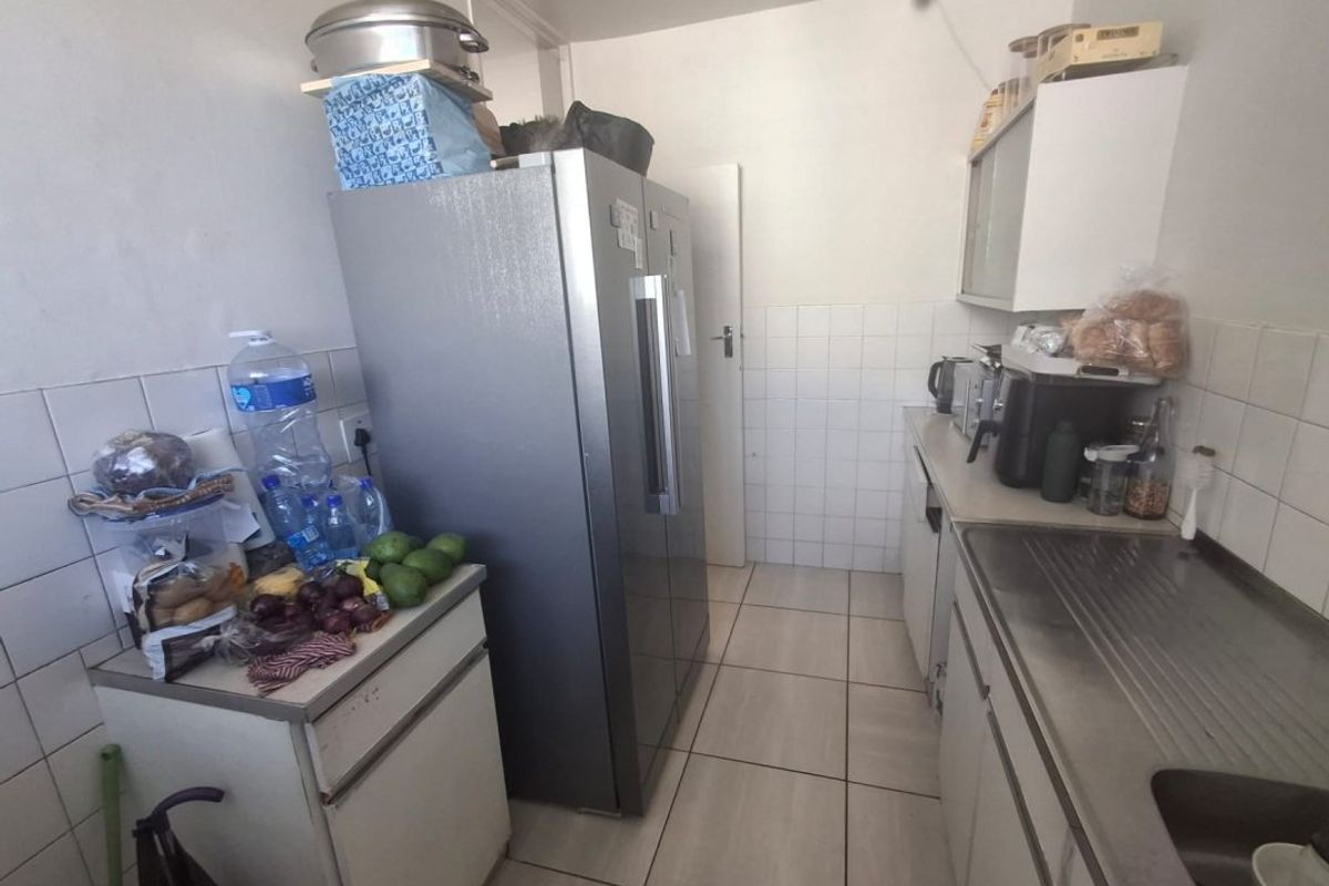 A compact kitchen featuring tiled splashbacks, stainless steel sink, and built-in cabinetry with tiled flooring.