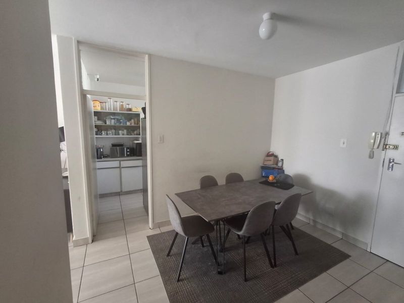 A dining area featuring neutral tiled flooring and an intercom system, with an open doorway leading into the adjacent kitchen space.