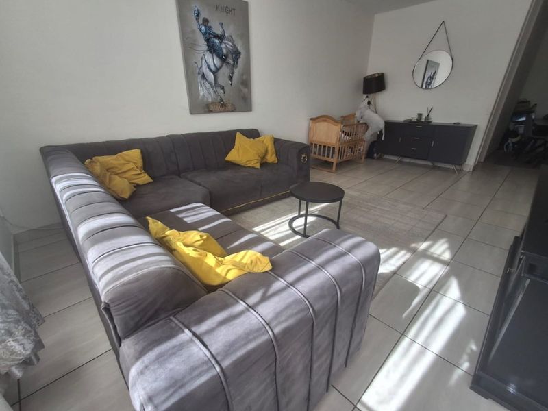 A living room area featuring neutral tiled flooring and ample natural light, providing a functional space for relaxation.