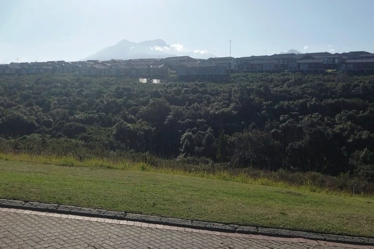A scenic view overlooking a lush green valley with a residential estate and mountain range in the background.