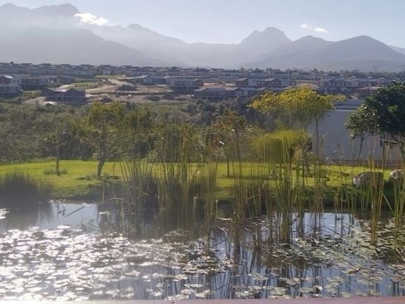 A scenic view overlooking a tranquil pond and landscaped garden with mountain vistas in the background.