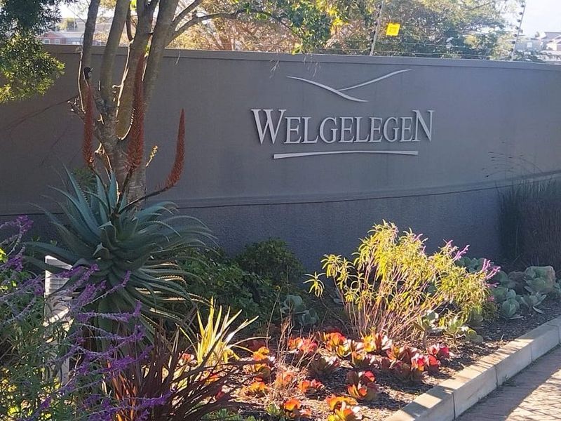 Entrance signage for Welgelegen estate, featuring a well-maintained boundary wall, landscaped garden beds, and secure electric fencing.