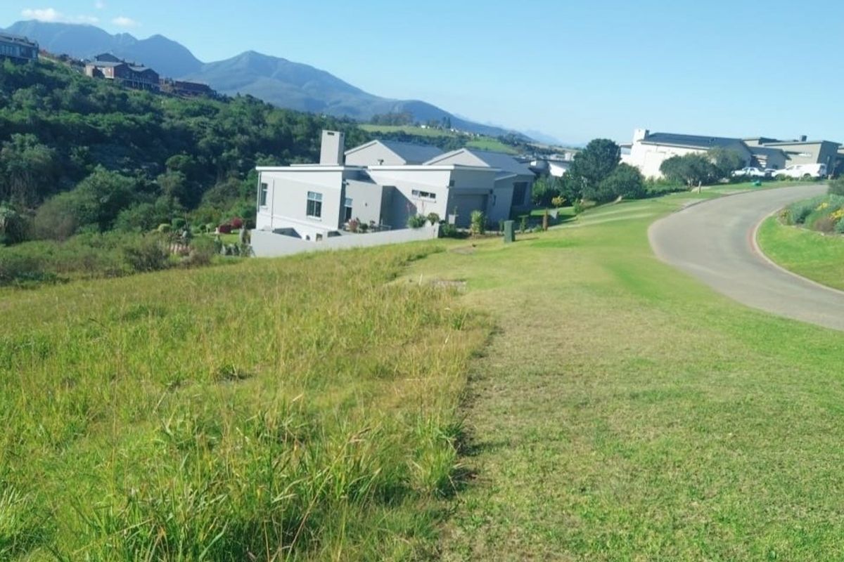 A view of a vacant residential plot of land situated next to a paved road in a developed estate.