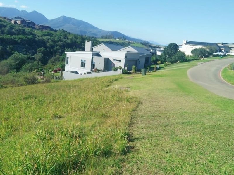 A view of a vacant residential plot of land situated next to a paved road in a developed estate.