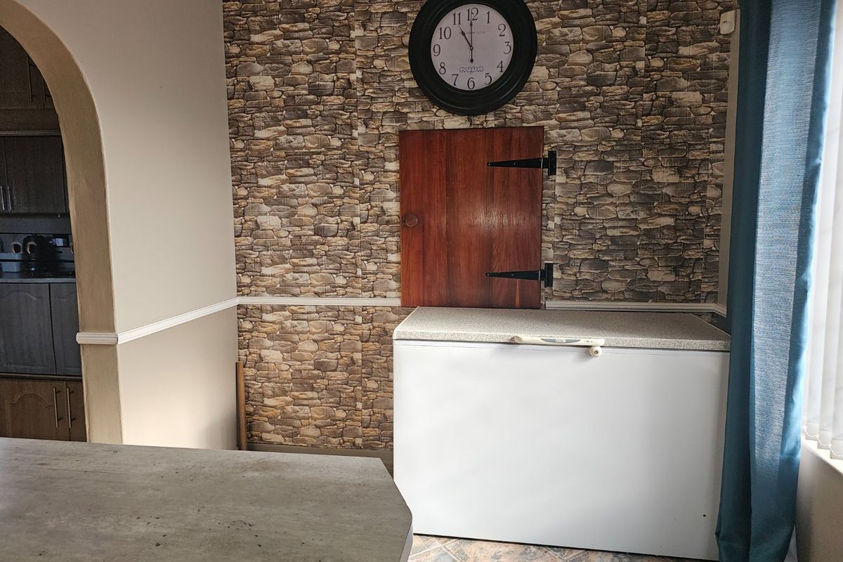 A kitchen area featuring stone-effect wallpaper, an arched entryway, and tiled flooring, providing a functional space with potential for modern updates.