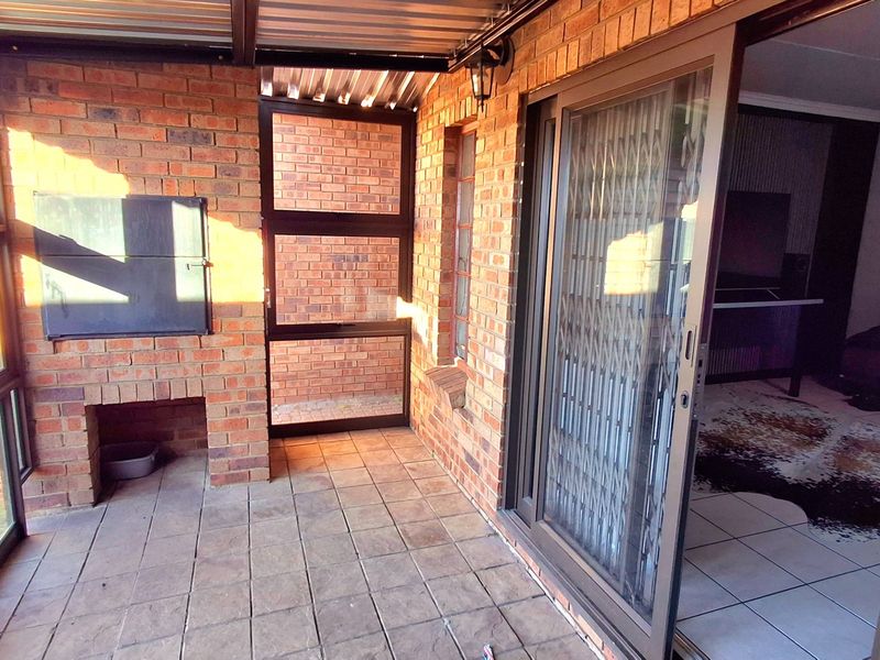 A covered patio area featuring exposed brick walls, a built-in braai, and sliding glass doors providing access to the interior living space.