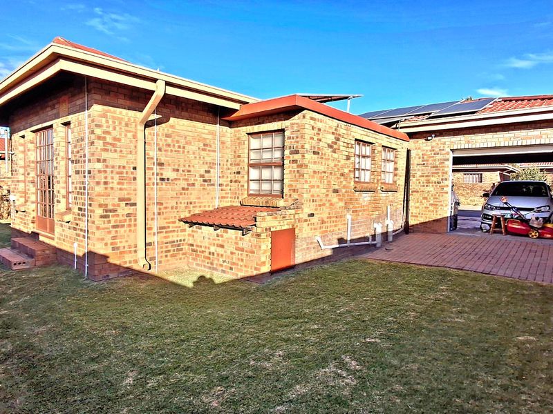 Rear view of a face brick townhouse featuring a tiled roof, solar panels, and an attached garage with a paved driveway area.
