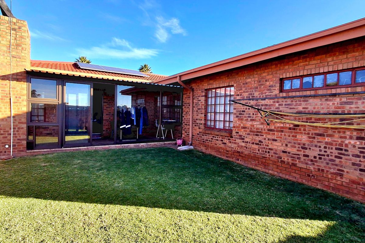 Rear exterior view of the townhouse featuring a brick facade, tiled roof with solar panels, and a private lawn area.