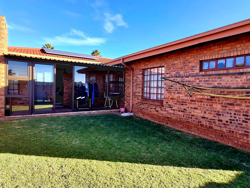 Rear exterior view of the townhouse featuring a brick facade, tiled roof with solar panels, and a private lawn area.