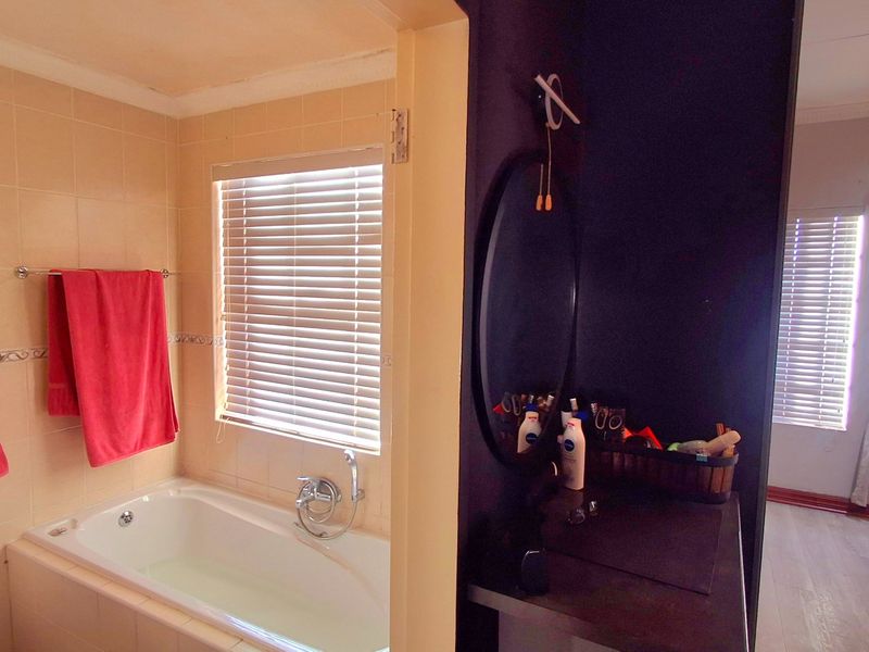 A bathroom featuring a built-in bathtub, wall-mounted basin, and tiled wall finishes, with an adjacent vanity area.