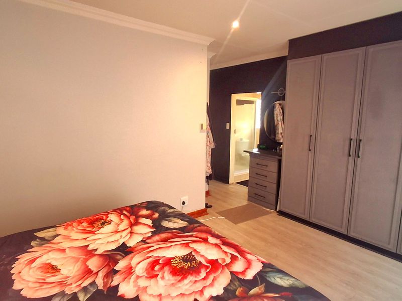 A well-maintained bedroom featuring modern grey built-in cupboards, light laminate flooring, and recessed ceiling lighting, with an adjoining en-suite bathroom visible.