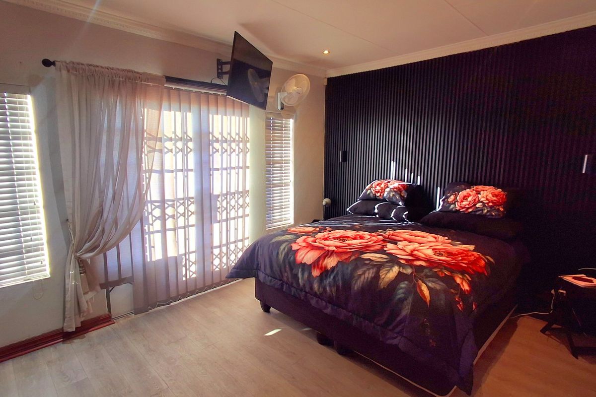 A well-maintained bedroom featuring a modern slatted accent wall, laminate flooring, and direct access to an outdoor area through a sliding door.
