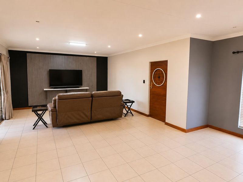 Spacious living room featuring neutral tiled flooring, recessed downlighting, and a modern slatted feature wall with direct access to the outdoor area.