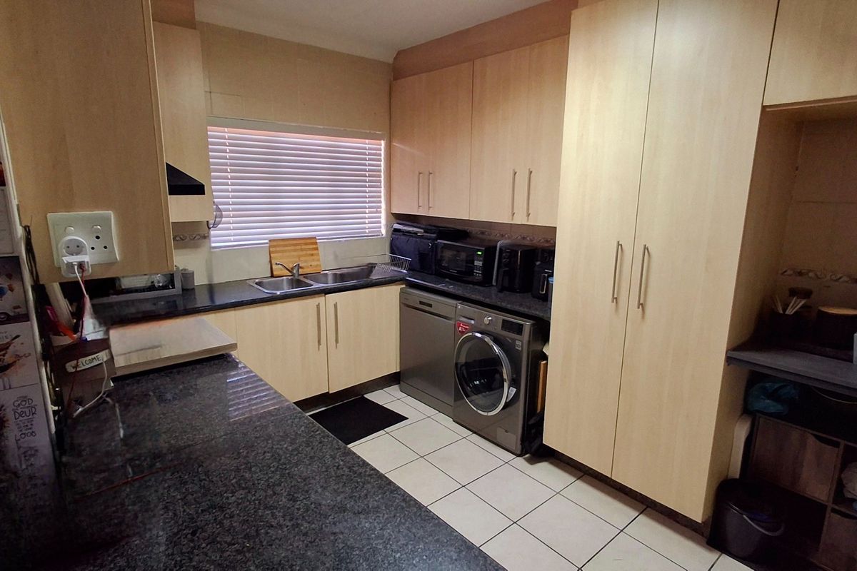 Functional kitchen featuring light wood-look cabinetry, dark granite countertops, ceramic floor tiles, and integrated space for laundry appliances.