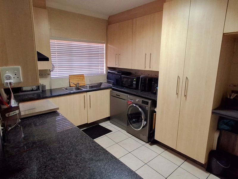 Functional kitchen featuring light wood-look cabinetry, dark granite countertops, ceramic floor tiles, and integrated space for laundry appliances.
