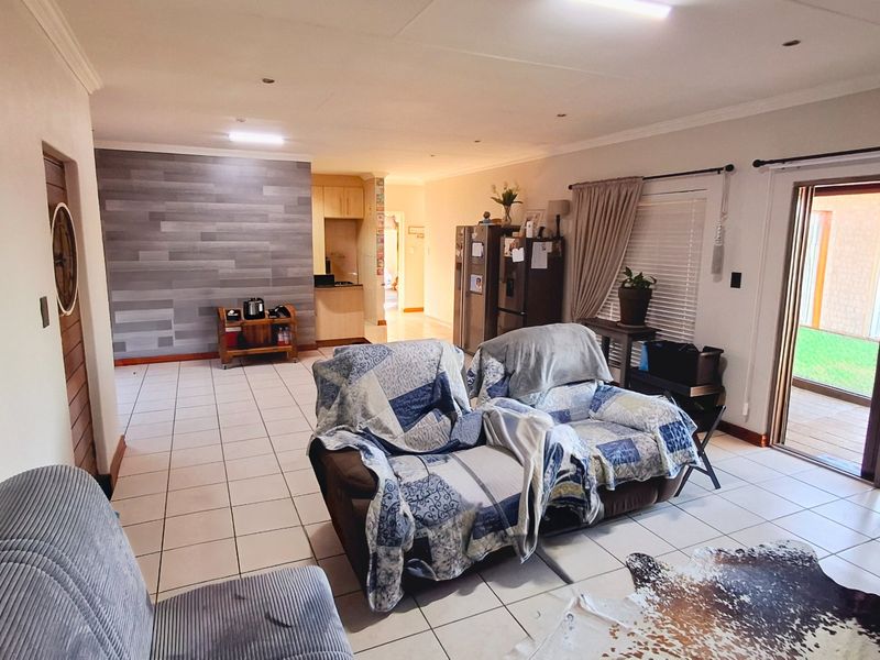 Spacious open-plan living area featuring tiled flooring, a decorative feature wall, and direct access to the outdoor patio through sliding glass doors.