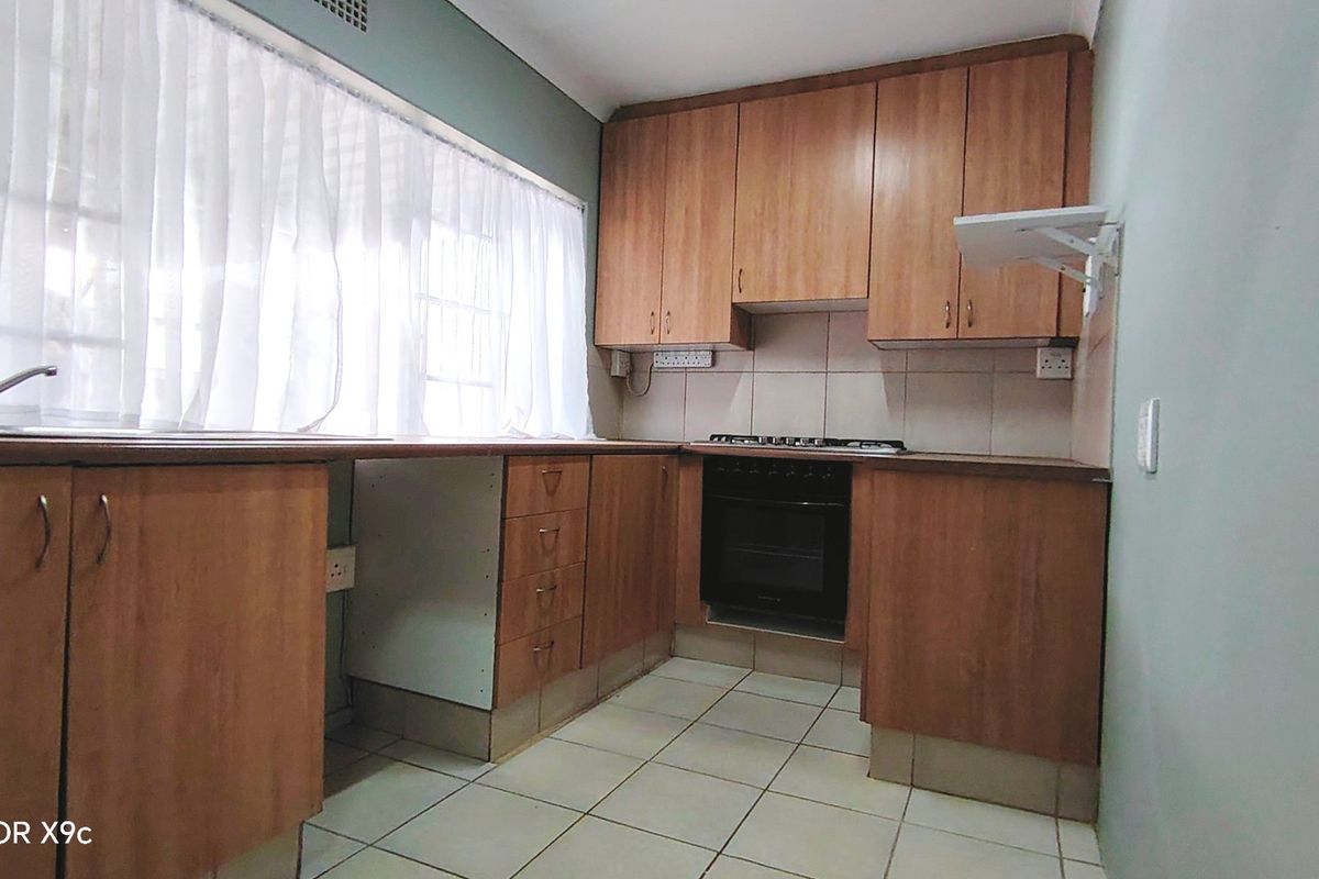 A functional kitchen featuring wood-look cabinetry, built-in oven with gas hob, tiled splashback, and ceramic floor tiles.