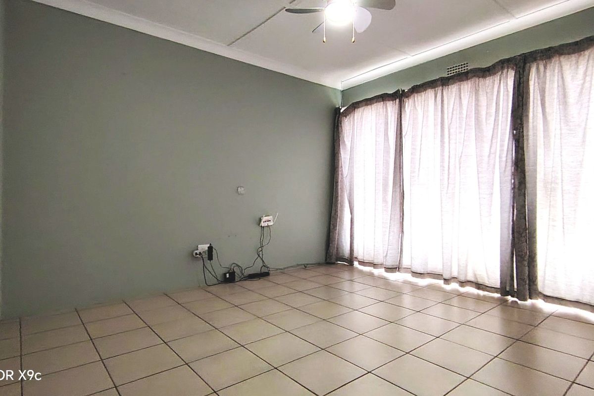 A spacious, empty living room featuring neutral tiled flooring, a ceiling fan, and large windows with curtain tracks, offering a blank canvas for styling.