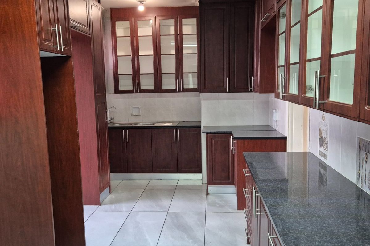 A clean, functional kitchen featuring dark wood cabinetry, granite countertops, and tiled flooring, offering a classic layout with ample storage space.