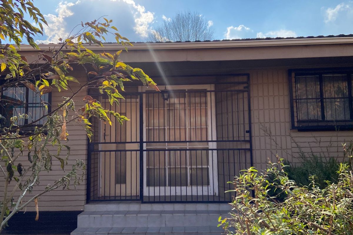 Rear exterior view of the house featuring a security gate, tiled entrance steps, and brick facade with window security bars.