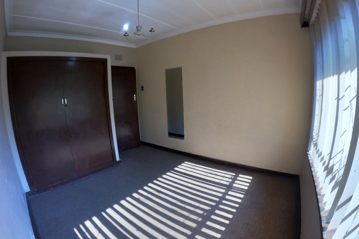 An empty bedroom featuring built-in wardrobes, carpet flooring, and vertical blinds, offering a neutral space ready for personalization.