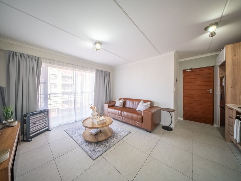 A bright open-plan living area featuring tiled floors, a modern kitchen with built-in cabinetry, and a sliding door leading to a balcony.