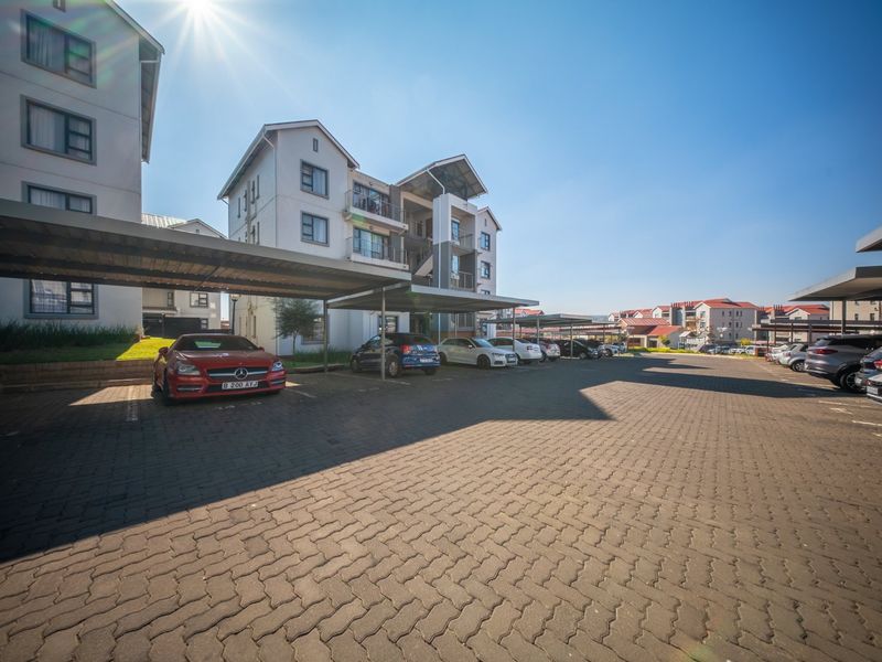 Exterior view of a multi-story apartment complex featuring paved parking areas with covered carports.