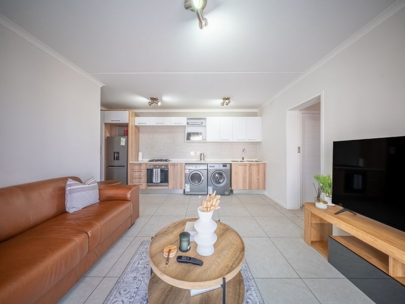Modern open-plan living area featuring a well-equipped kitchen with built-in cabinetry, integrated appliances, and neutral tiled flooring throughout.