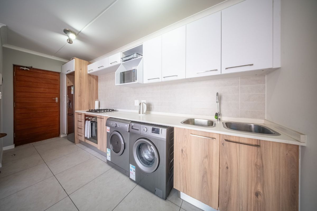 Modern kitchen featuring light wood and white cabinetry, gas hob, built-in oven, microwave, and double stainless steel sink with tiled flooring.