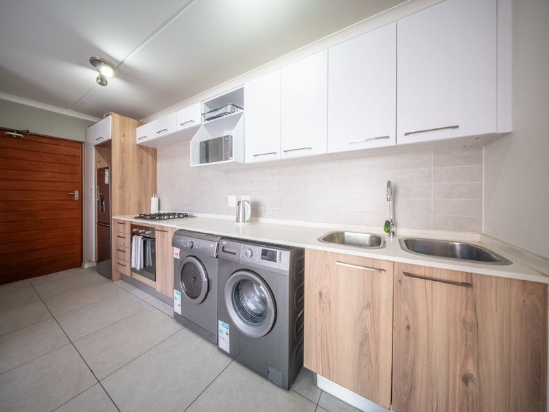 Modern kitchen featuring light wood and white cabinetry, gas hob, built-in oven, microwave, and double stainless steel sink with tiled flooring.